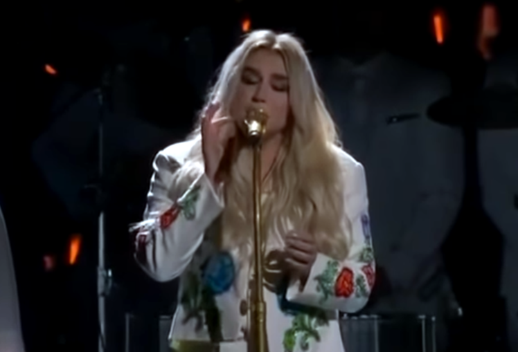Kesha performing behind a microphone, performing "Praying" at the 2018 Grammys.