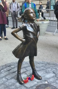 Photo of bronze statue of girl standing with hands on hips and looking up. 