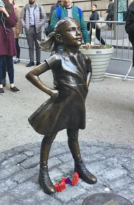 Photo of bronze statue of girl standing with hands on hips and looking up.