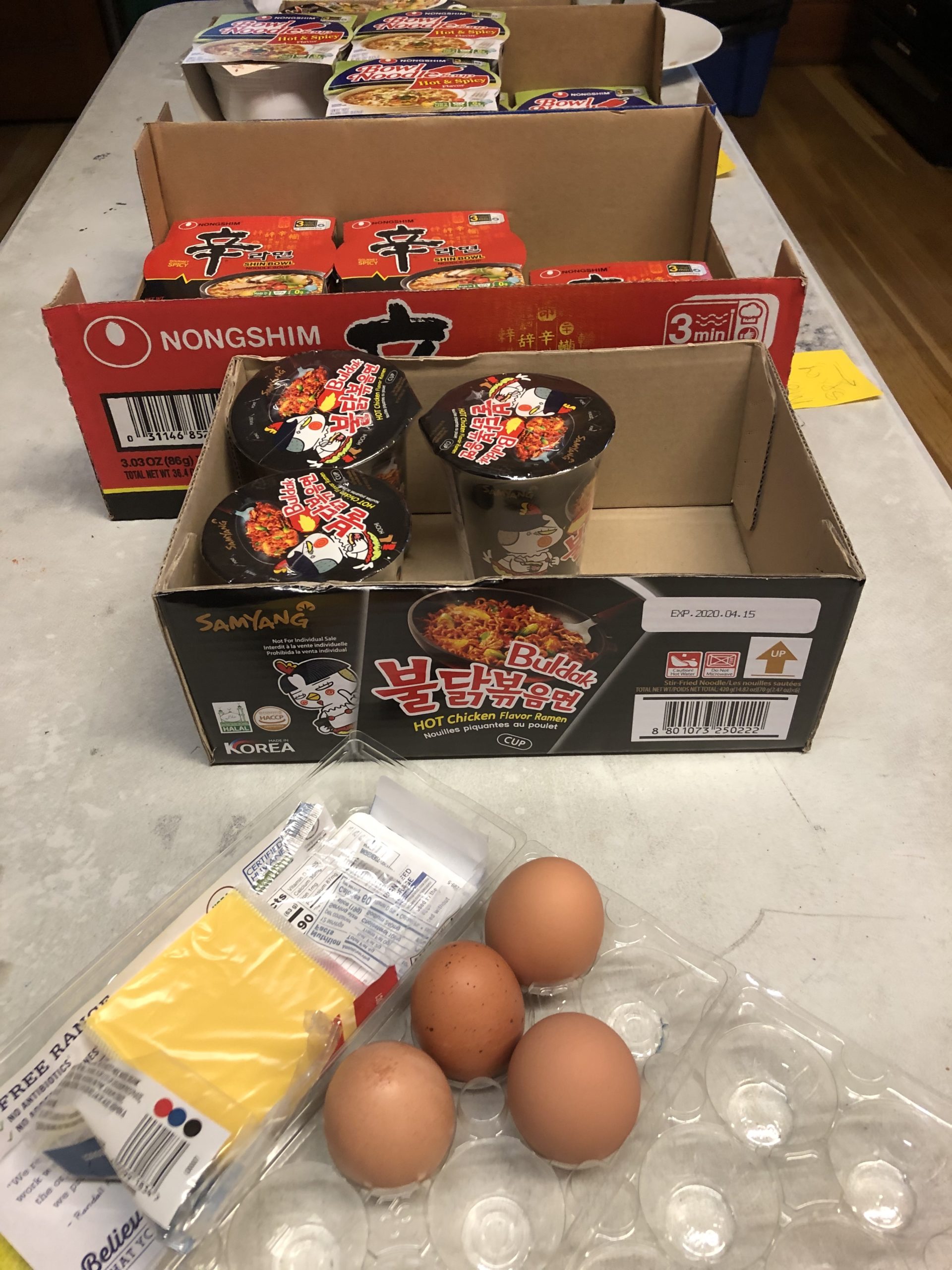 Photo of three different Instant Noodle packages and carton with four brown eggs.
