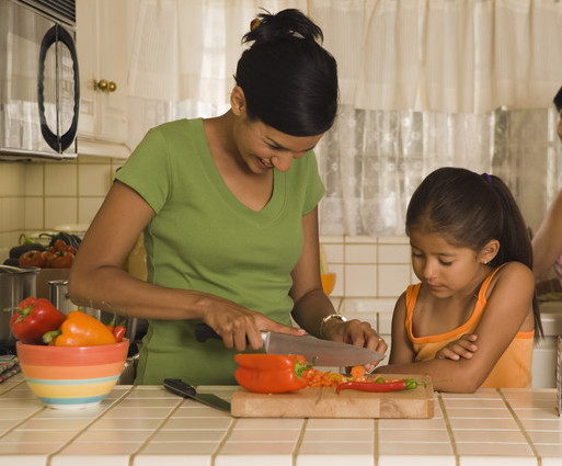 Image of mother and daughter in kitchen. Mother is cutting peppers while daughter stands next to her, watching.