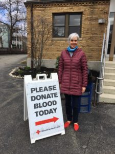 Photo of woman standing next to sign. Text on sign: "Please donate blood today."