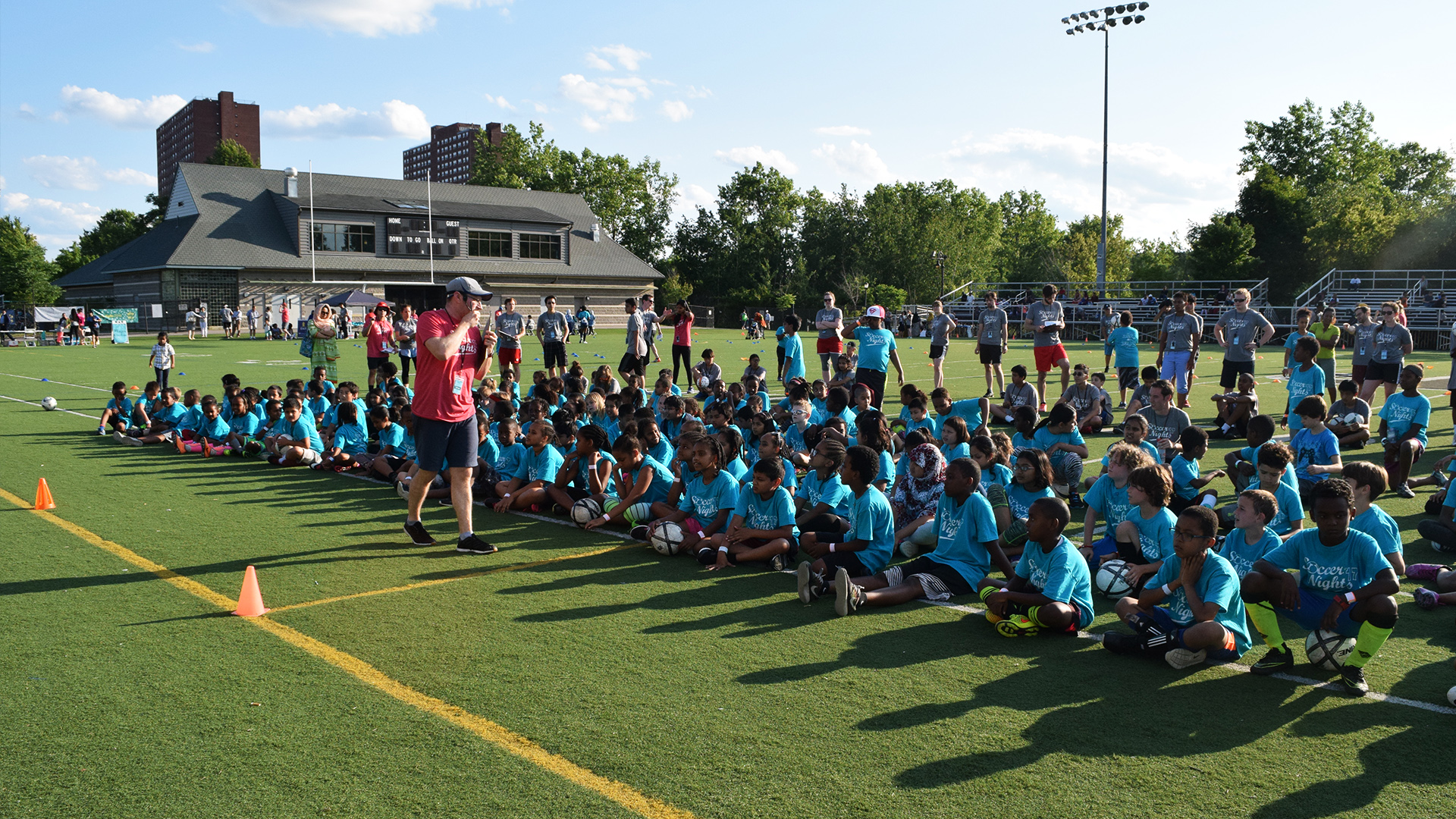 Photo of soccer field with a large group of kids sitting on field.